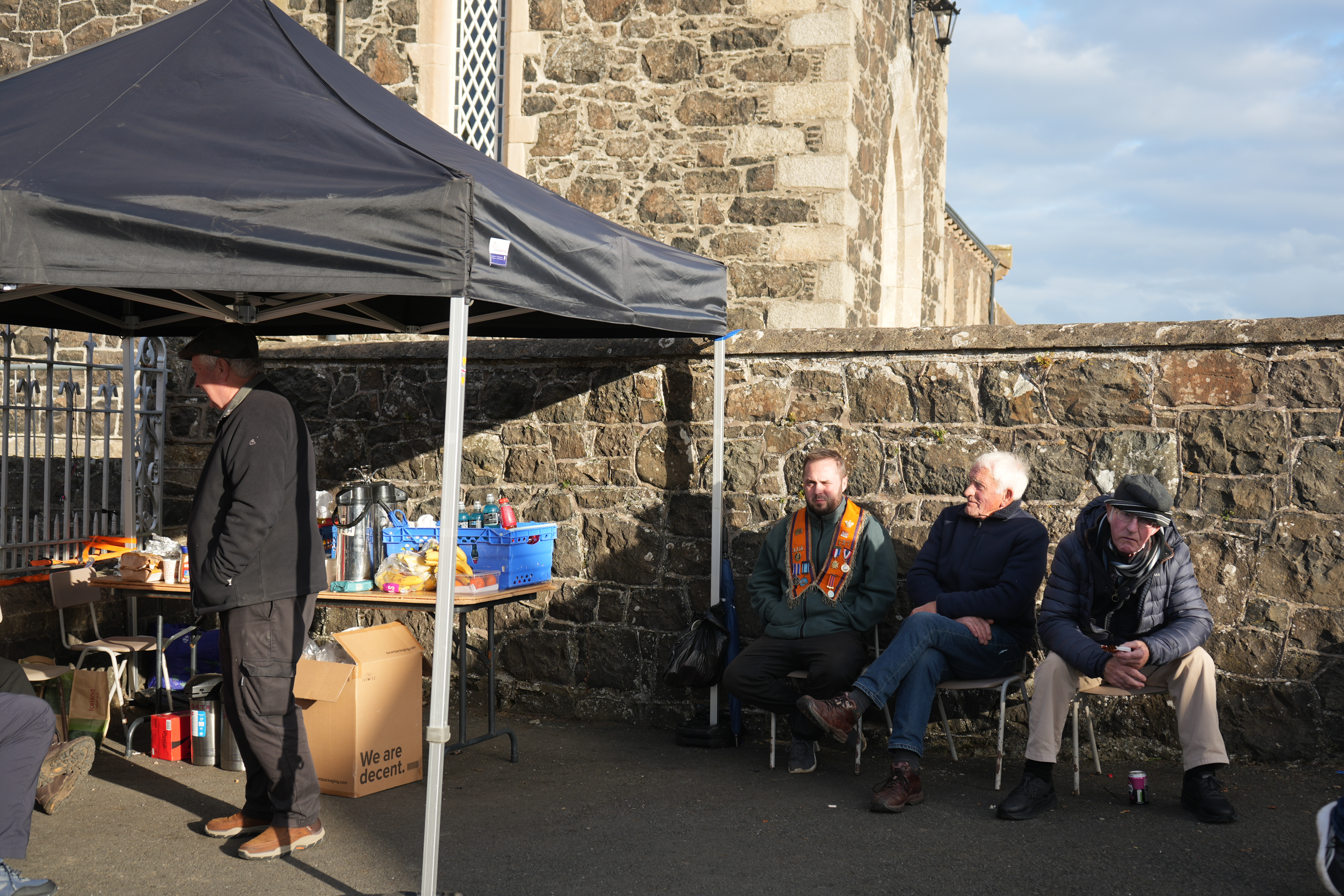 Orange Order members sit outside Drumcree church as they await passage along Garvaghy Road in Portadown, Northern Ireland, on October 1, 2026 [Caolán Magee]