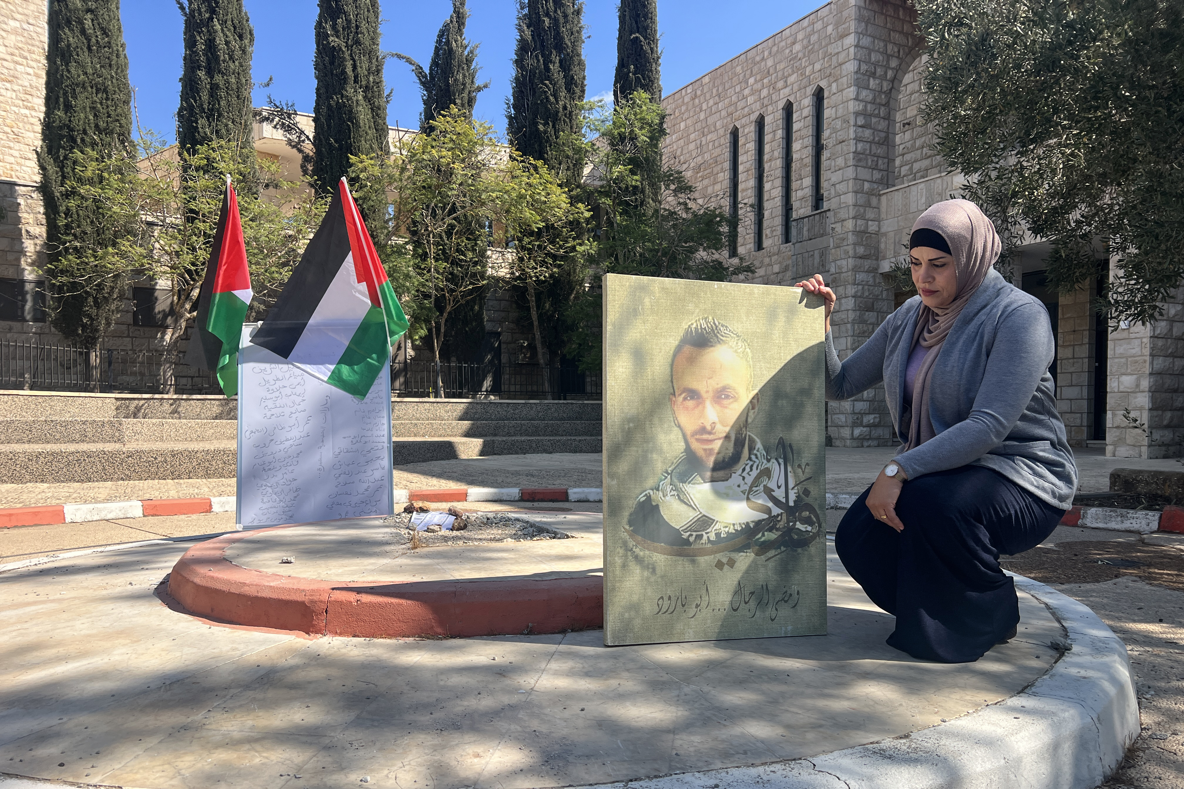 Rania Washaha is holding her brother’s photo near the memorial in BZU