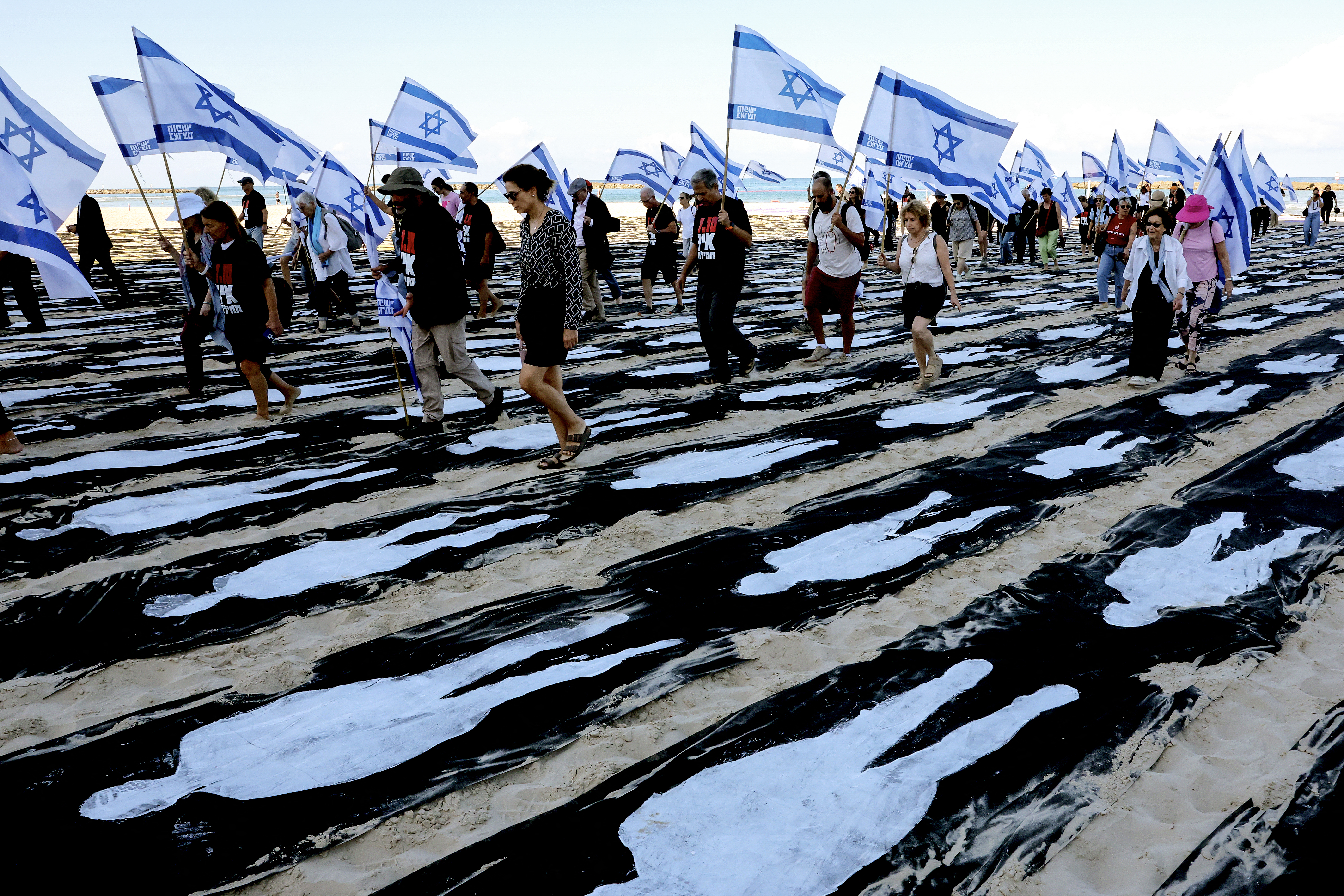 People carrying Israeli flags walk through a commemorative installation set up on the beach in Tel Aviv to mark the third anniversary of Hamas's October 7 attack on Israel, on October 7, 2026.