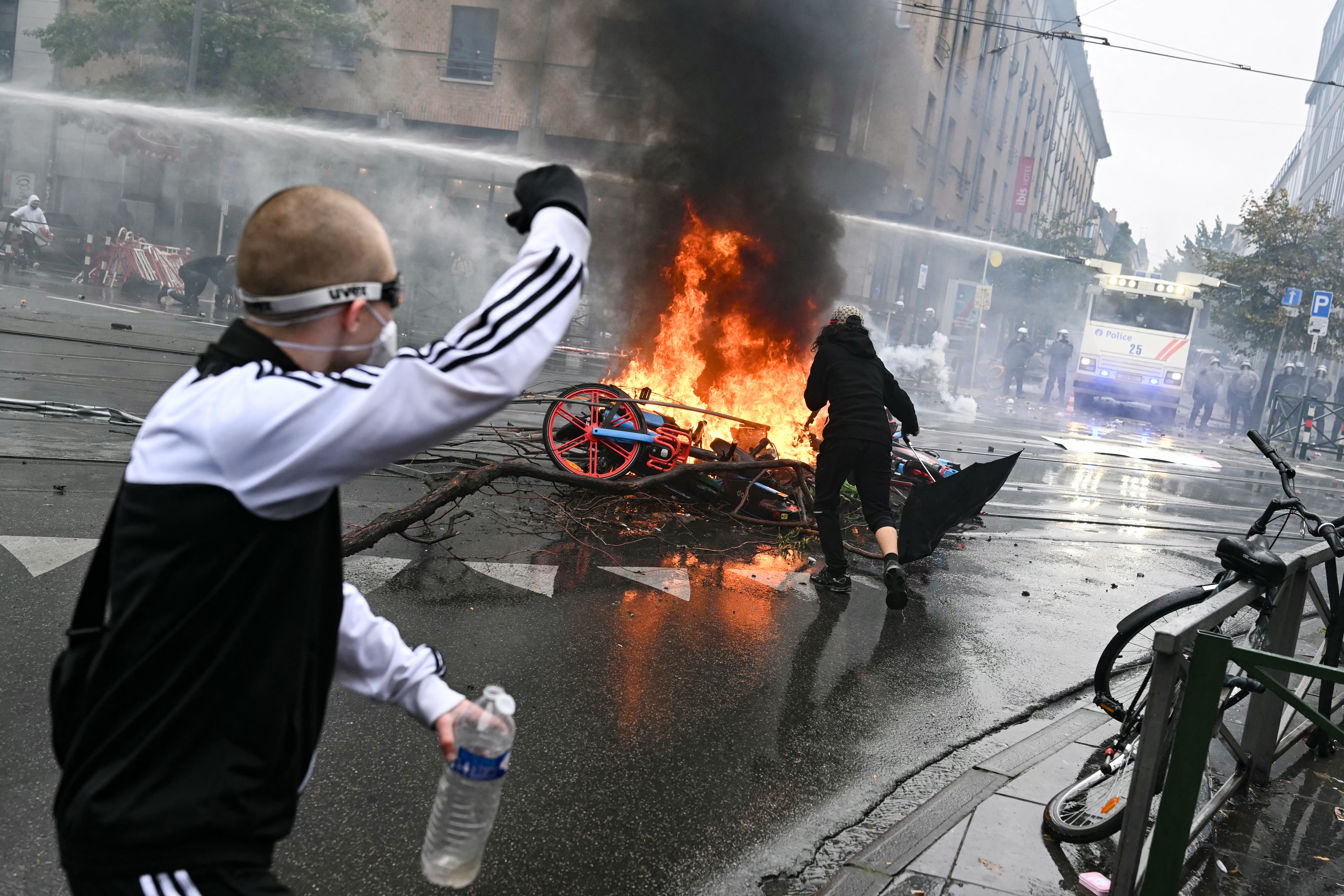 A protester gestures next to burning shared bikes during a labour union-based demonstration against the Federal Government's budgetary measures near the Brussels-South railway station in Brussels on October 9, 2026.