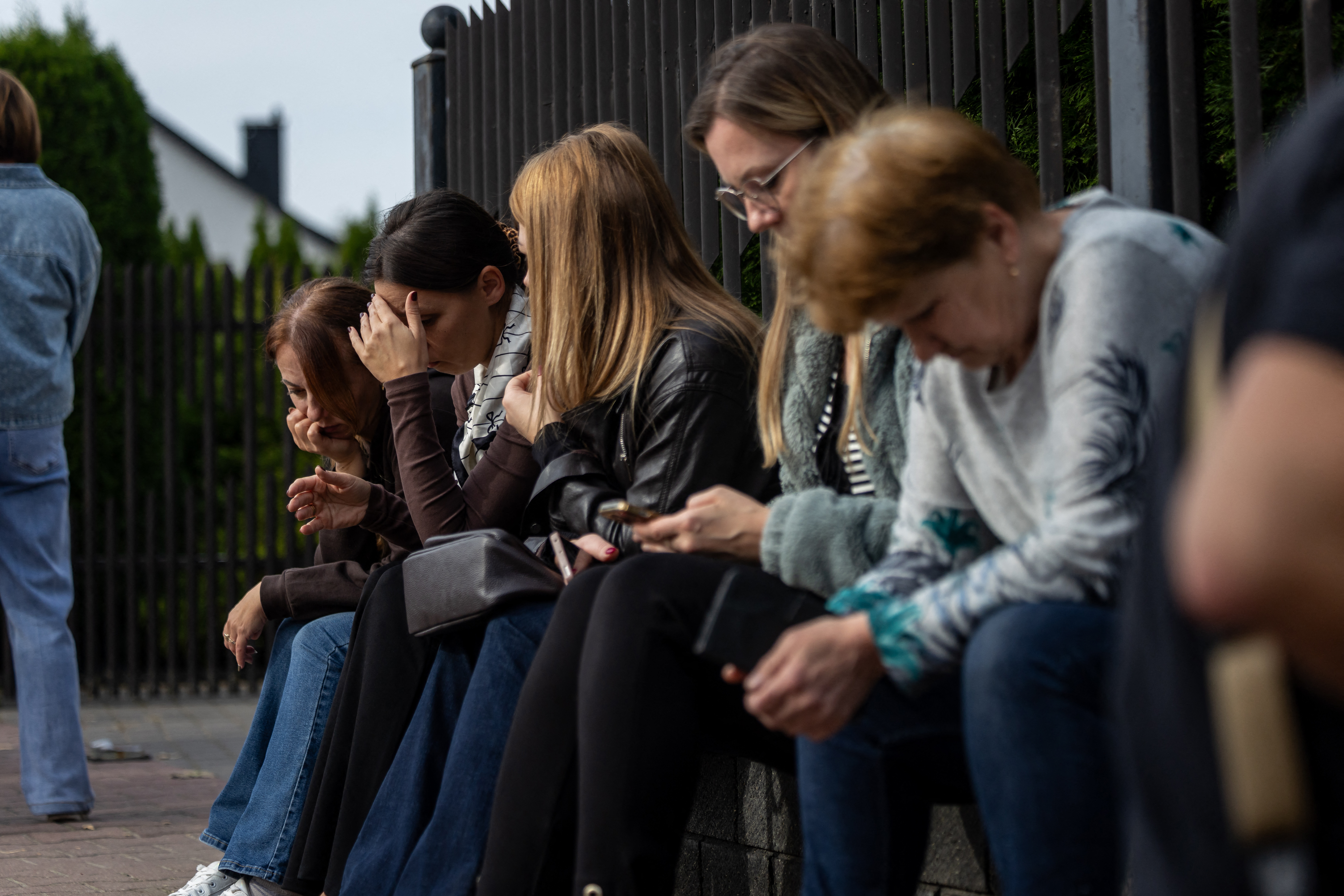 Local residents wait next to the scene where a 15-year-old fatally stabbed the caretaker of his former school and wounded two other adults at the John-Paul II primary school in Leszczydol-Nowiny, Poland, on October 8, 2026, a day after a similar knife attack wounded nine in a Polish high school, police said.