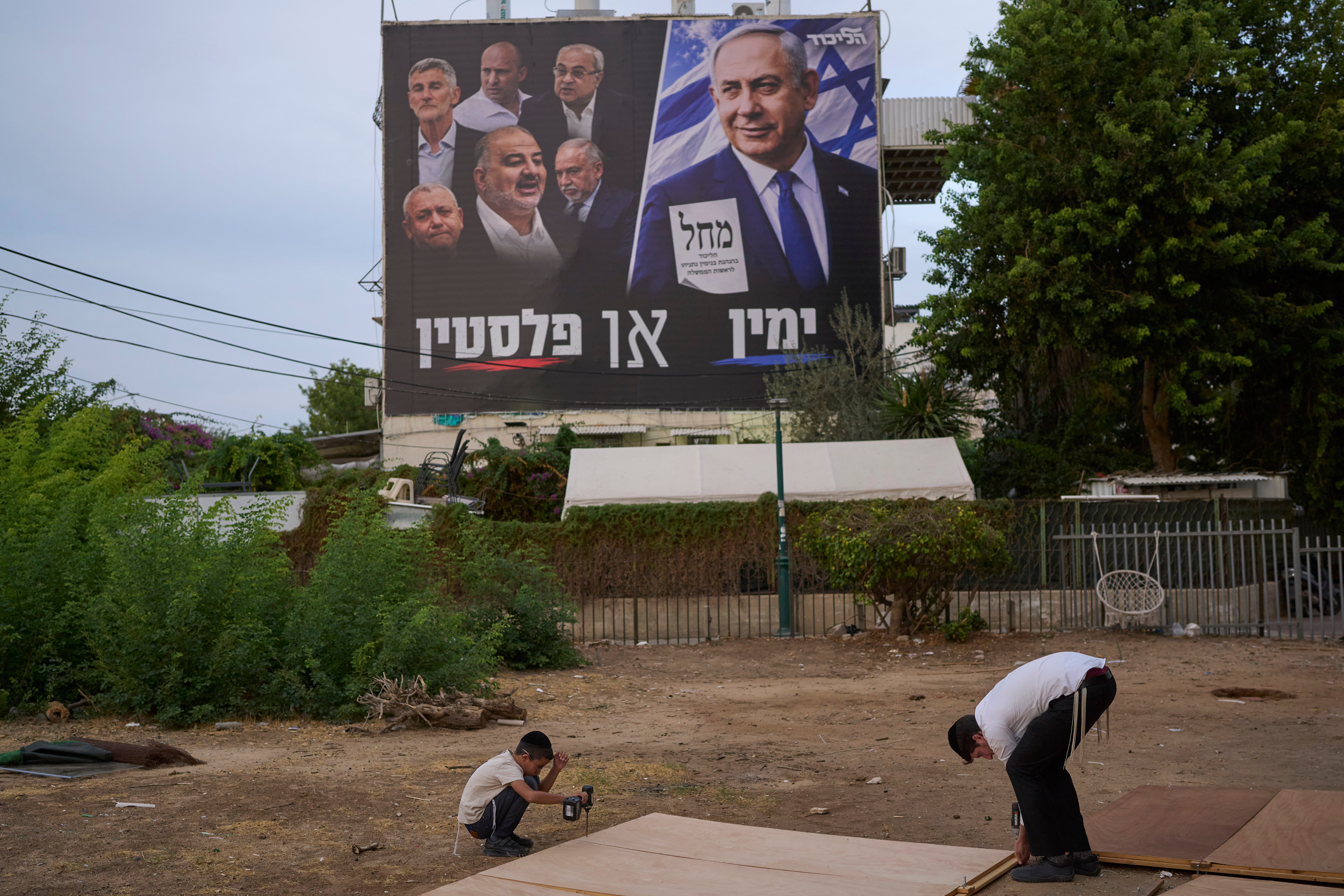 Ultra-Orthodox Jewish men stand next to a billboard depicting Israeli Prime Minister Benjamin Netanyahu alongside leaders of opposition parties, with the slogan 'Right or Palestine'.