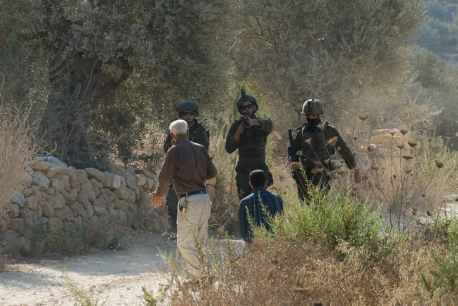 An Israeli soldier aims a weapon at Palestinians at Palestinian-owned olive groves during the harvest season in the village of Beita near Nablus, in the Israeli-occupied West Bank, October 3, 2026. REUTERS/Mohamad Torokman