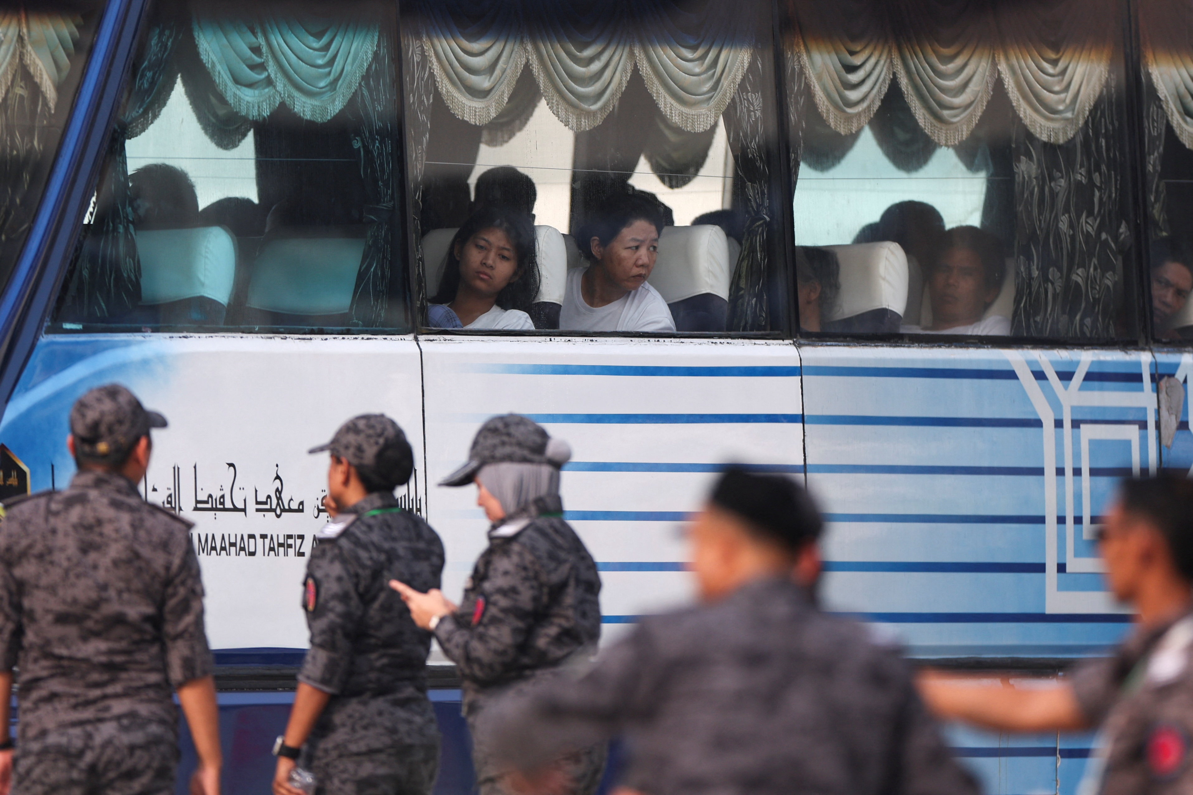 People sit inside a bus as personnel in army uniforms look on.