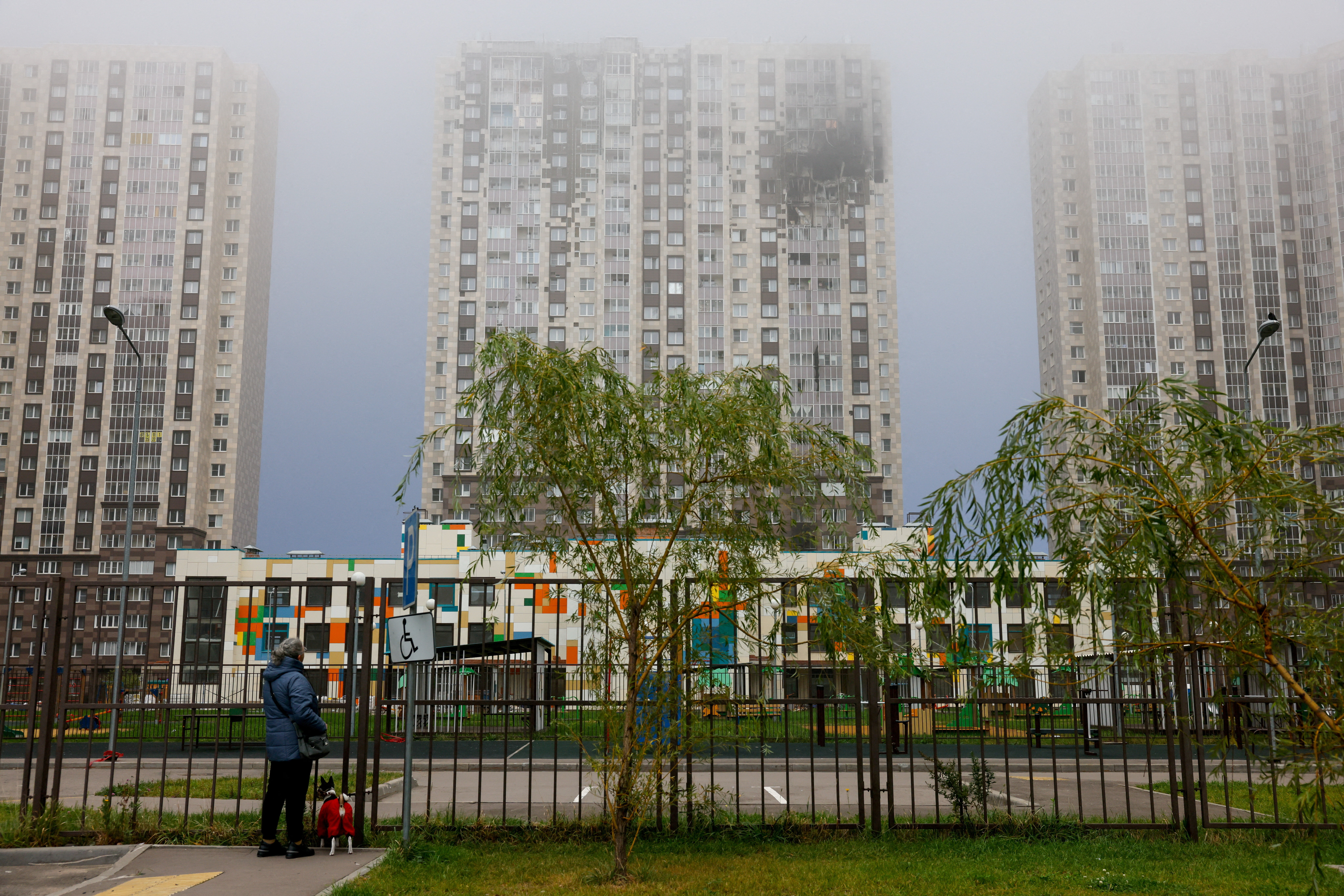 A woman with a dog looks at a damaged multi-storey residential building hit by what authorities described as a Ukrainian drone strike, amid the Russia-Ukraine conflict in Kotelniki in the Moscow region, Russia, September 20, 2026. REUTERS/Stringer TPX IMAGES OF THE DAY